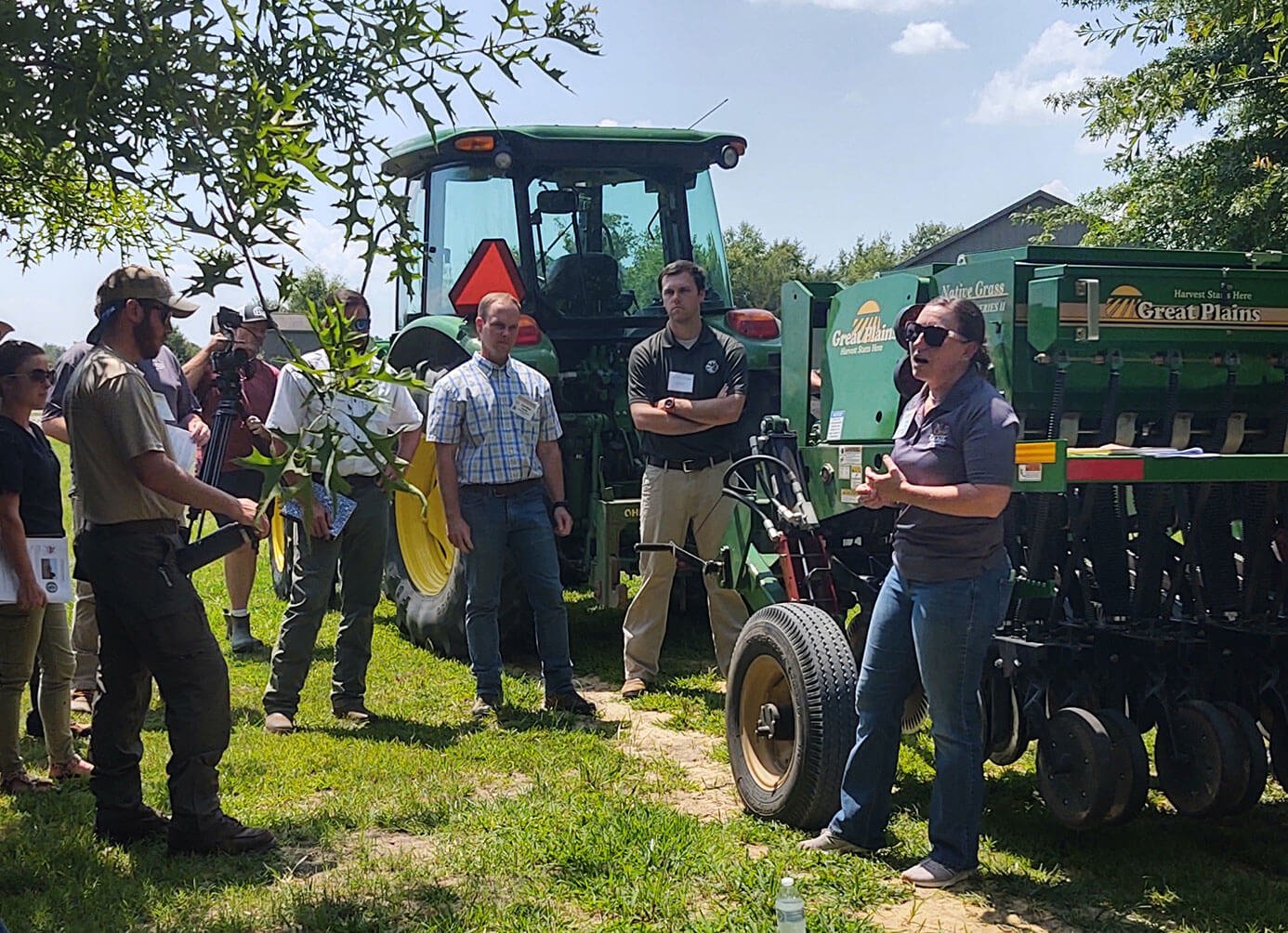 Person talking to a group of people in a field next to field equipment