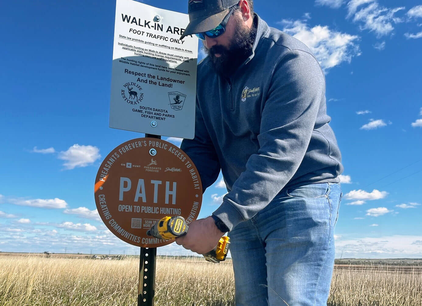 Worker in field with blue sky next to PATH sign 